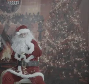 Santa doing karate moves whilst on a chair in front of a christmas tree image